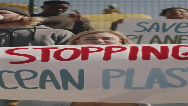 Vertical shot of woman holding poster with Stopping Ocean Plastic sign, looking at camera and hanting slogan while protesting with environmental activists against pollutionVertical shot of woman holdi