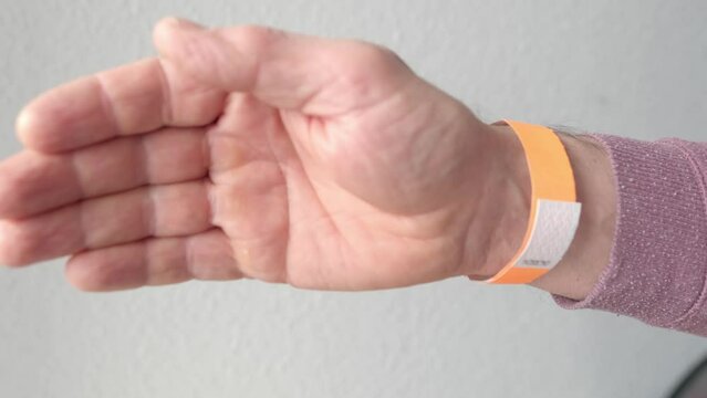 orange paper wristband mockup on persons arm. Clear adhesive bangle wristlet sticker with entry number on male hand of middle-aged european man, blue paper bracelet, check tape, event ticket concept