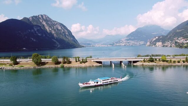 Melide, Switzerland: A cruise boat sails under the Melide bridge on lake Lugano in Canton Ticino in Switzerland. 
