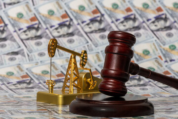 A miniature oil pump and a judge's gavel against the background of 100 US dollar bills