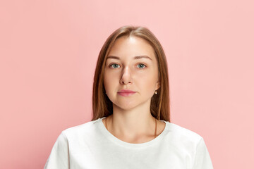 Portrait of young beautiful woman wearing white t-shirt, posing, looking at camera against pink studio background. Calm face, straight look