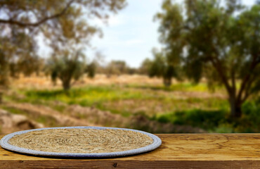 Detail view of  round trivet made of wicker on wooden board near blur olives field