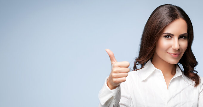 Businesswoman in confident white suit, showing thumbs up gesture, copy space area for some text, advertising or slogan, over grey color background. Business concept photo.