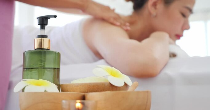 Close up items and accessories for massage. Background asian woman relaxing with massage while laying on bed. Oil bottle, Flowers, Scrub sugar or salt. Wellness center, Healthy Concept