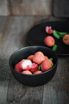 Fresh ripe lychee fruit and peeled lychee with green leaves on wooden background. Rustic style