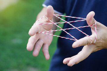 Closeup boy hands is playing rope which called cats cradle game. Concept, game involving the creation of various style figures between the fingers. Traditonal playing. - obrazy, fototapety, plakaty