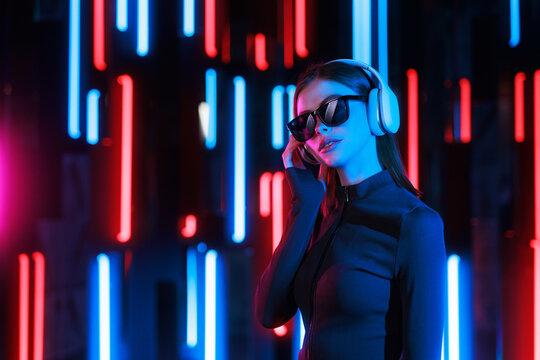 Beautiful woman with purple hair in futuristic costume over dark background. Violet neon light. Portrait of young girl in modern headphones listening music.