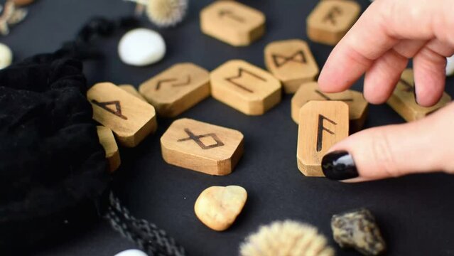 Scandinavian wooden runes in the hands of fortune teller on black table with velvet bags and stones. Magic esoteric symbols for divination and prediction of the future and destiny, esotericism.