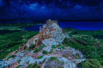 Iconic view of Volterraio Castle on rock at 394 m. Fortress of Volterraio, symbol of Elba Island, dominates Portoferraio Gulf. Volterraio castle by night with milky way, stars field and galaxies.