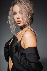 Naklejka premium portrait of sexy fashion-forward woman in lace bra and panties posing and looking at camera on grey background, dyed ash blonde hair, expressive gaze, femininity and modern style