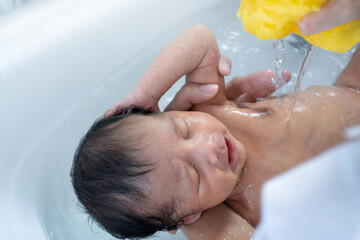 Asian newborn baby bathing in bathtub, flow water into baby with yellow sponge, newborn baby care concept