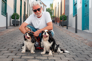 Portrait of smiling senior white haired man posing in the street with his two cavalier king charles...
