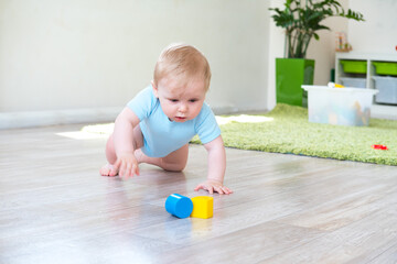 Cute baby in blue clothes crawling on floor with toys