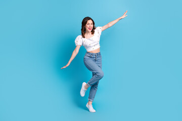 Fototapeta na wymiar Full length photo of adorable carefree girl dressed white top flying arms sides isolated blue color background