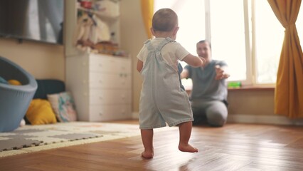 baby first steps. baby goes to her father at window learns to walk to take first steps. happy family kid dream concept. dad calls son baby first steps indoors. happy family lifestyle indoors concept - obrazy, fototapety, plakaty