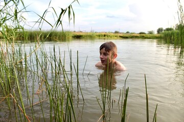 one boy sits in the river in the water rests in the summer on vacation in the village and looks at the reeds with admiration