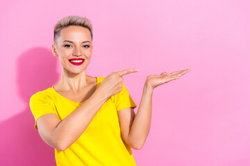 Photo of cheerful lovely girl toothy smile indicate finger arm hold empty space isolated on pink color background