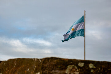 Fototapeta premium Light blue and white Argentinian flag waving with blue sky and grey clouds as background