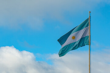 Light blue and white Argentinian flag waving with blue sky and grey clouds as background