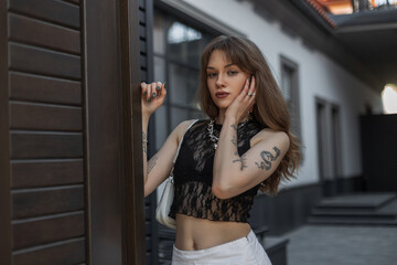 Fototapeta na wymiar Fashionable beautiful hipster girl with a tattoo on her arms in fashion summer clothes with a stylish black lace top in the city