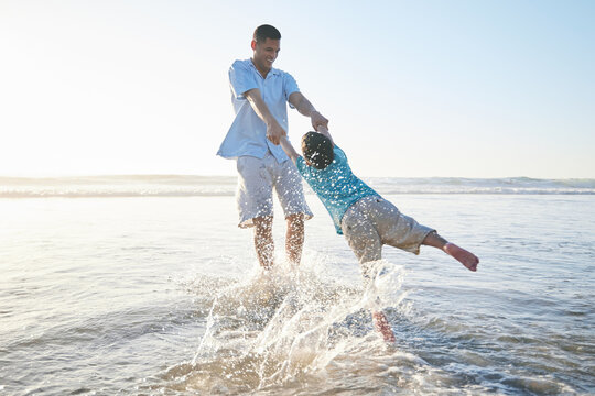 Beach, family and father and spinning a child for fun, adventure and play on holiday. A man and young kid holding hands on vacation at the ocean, nature or outdoor with water splash and freedom