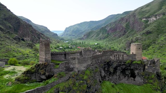 Dramatic drone shot of a medieval castle overlooking a lush green mountain valley in Georgia