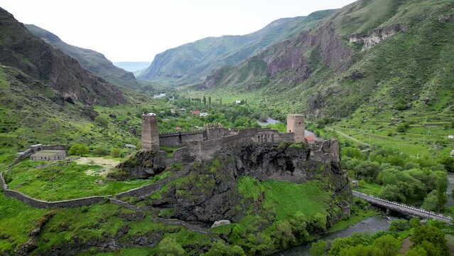 Dramatic drone shot of a medieval castle overlooking a lush green mountain valley in Georgia