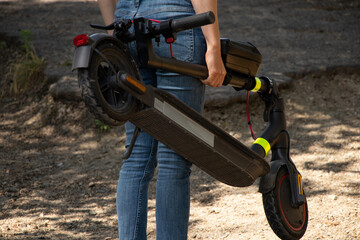 Obraz premium A girl holds an electric scooter in her hands in parks in Ukraine in the summer, urban transport