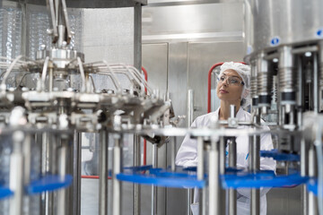 Female worker inspecting quality clean purified drinking plastic water bottles on machine drinking water bottling plant during manufacturing processing. Manufacturer and Inspection quality control