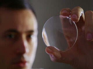 Young man holding glass lens eyewear for quality control glasses manufacturing
