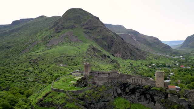 Dramatic drone shot of a medieval castle overlooking a lush green mountain valley in Georgia