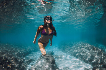 Woman in bikini snorkeling underwater in blue sea.