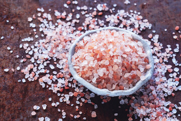 Himalayan pink salt in white ceramic plate on rusty table background.