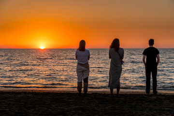 Three people watching the sunrise on the sandy beach in the capital of Dagestan Republic in the southern Russia