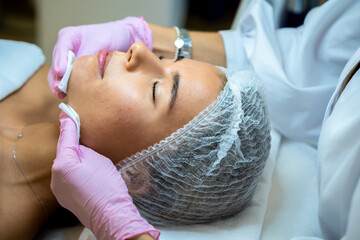 Female beautician doctor cleaning customer skin, make facial massage to patient.