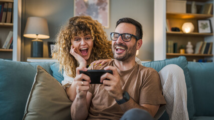 couple man and woman husband wife play smart phone video games at home