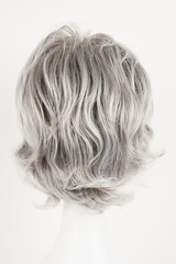 Fototapeta premium Natural looking silver blonde wig on white mannequin head. Short hair on the plastic wig holder isolated on white background, back view