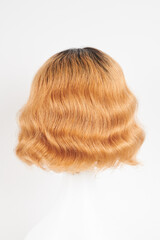 Fototapeta premium Natural looking ginger wig on white mannequin head. Medium length hair with wavy curls on the plastic wig holder isolated on white background, back view.
