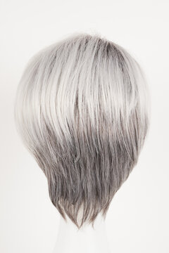 Natural looking silver blonde wig on white mannequin head. Short hair on the plastic wig holder isolated on white background, back view