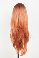 Naklejka premium Natural looking ginger wig on white mannequin head. Long straight hair with wavy curls on the plastic wig holder isolated on white background, back view.