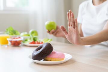 Diet, dieting, happy asian young woman, girl hand push out, deny sweet donut or dessert doughnut on plate, choose green apple and vegetable salad, eat food for good healthy, female getting weight loss