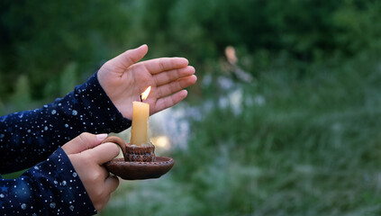 woman hands with burning candle in candlestick outdoor, abstract natural background. magic,...