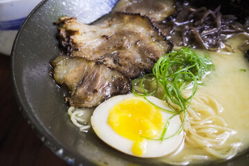 Close-up photo of Japanese pork miso ramen consisting of broth, miso, pork, sliced scallions, sliced mushrooms, soft half boiled egg or ajitsuko tamago ajitama in a bowl on a wooden table.