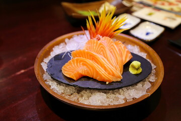 Close-up shallow focus of salmon sashimi beautifully arranged on a stone slab. There was wasabi next to it. and flower ornaments on ice mounds in round bowls. Beautifully arranged, blurred background.