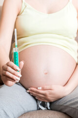 syringe for injection in pregnant woman's hand on sofa at the home, Healthy millennial healthcare concept