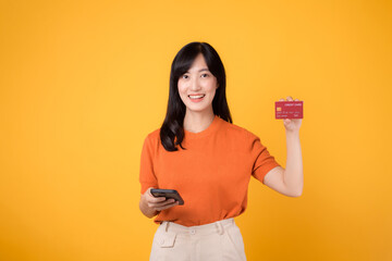 portrait cheerful young 30s asian woman happy smile holding credit card for purchase online shopping payment on smartphone isolated on yellow background.