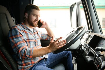 Young professional driver communicating over mobile phone while driving a truck.