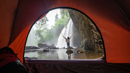 Fototapeta na wymiar Asian female tourists camping in a cave in the middle of the forest To experience the atmosphere of a waterfall in tropical forest area of Thailand. Asian woman camping to see a beautiful waterfall.