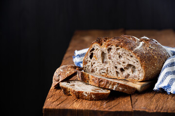 Rustic sourdough bread with cut slices on a wooden table. Black background with free space for text.