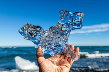 Transparent piece of ice with colorful reflections in the hand of a tourist traveling in Iceland